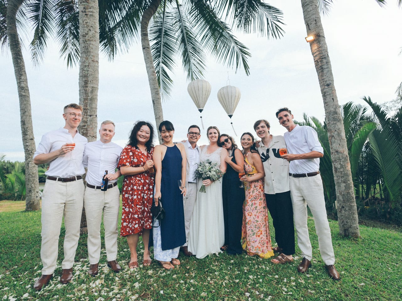 Bride and wedding guests posing for a group photograph beneath palm trees
