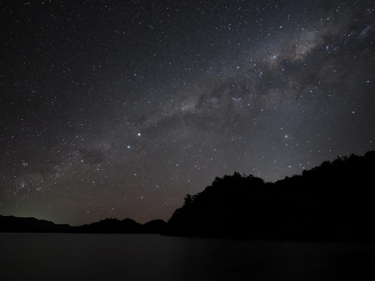 The Milky Way stretching above dark hills and water